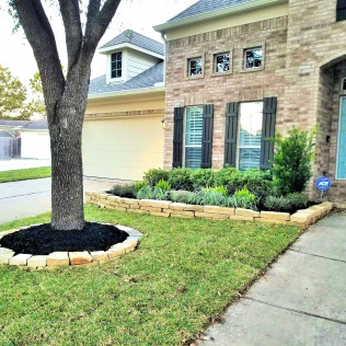 House with brick facade, front yard with tree and landscaped flowerbed.