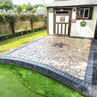 Brick patio with a star design, bordered by gray pavers and black gravel, next to a shed.
