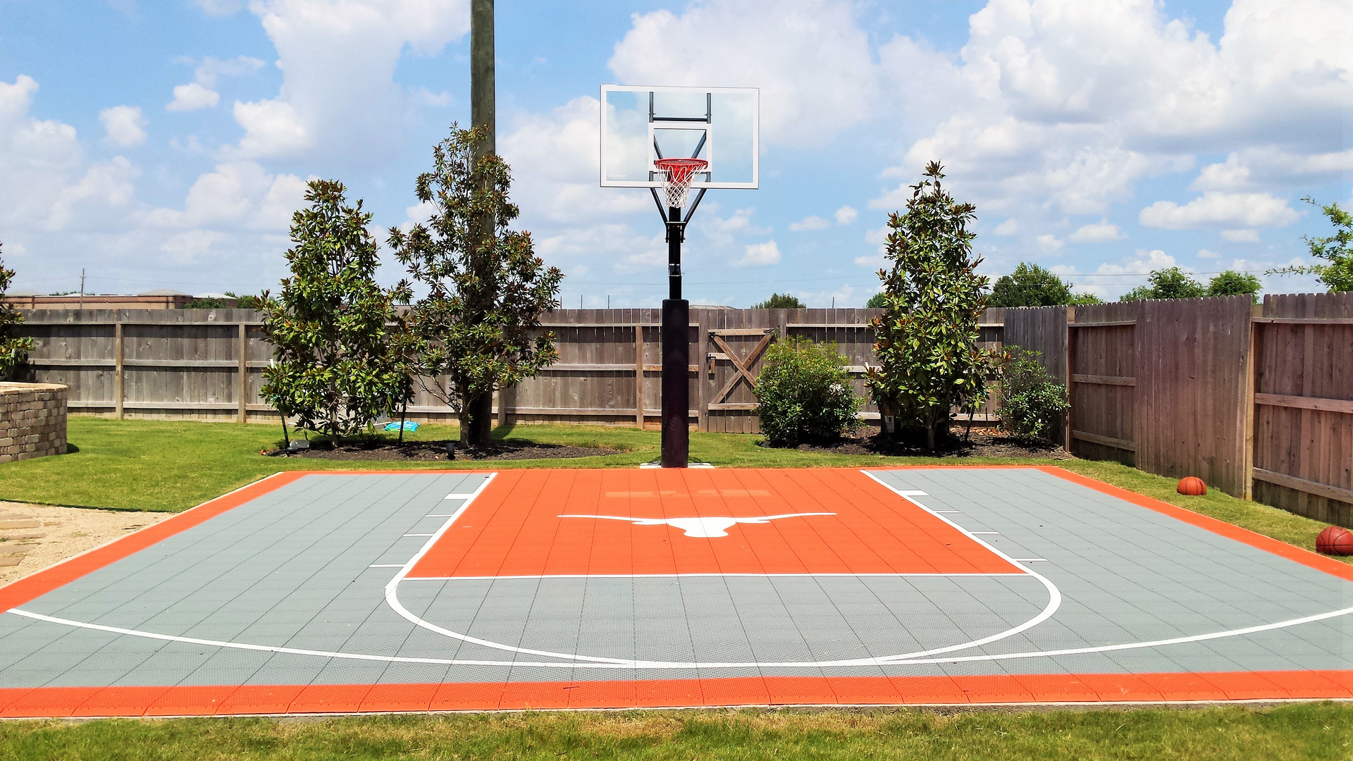 Basketball court with orange and gray tiles, Texas Longhorns logo, and clear sky.