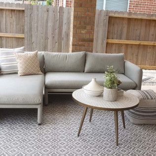 Outdoor patio with gray sectional, patterned rug, coffee table, and decorative pillows.