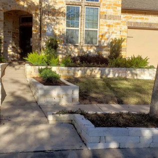 Stone-walled flowerbeds and ramp leading to a house entrance with greenery.
