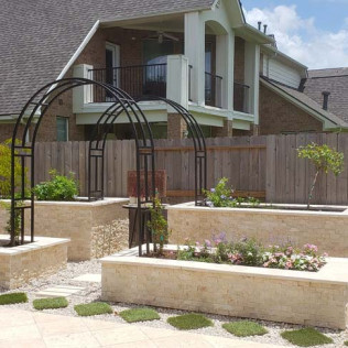 Black arched garden structures above rectangular flowerbeds, with house in background.