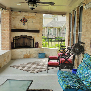 Outdoor covered patio with stone fireplace, seating, and view of houses.