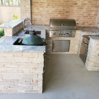 Outdoor kitchen with built-in grill, Big Green Egg, sink, and stone facade.