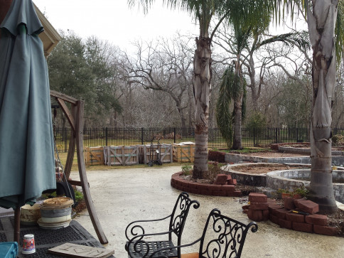 Patio with ornate chairs, umbrella, and a view of trees and a fenced area.