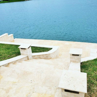 Stone steps leading down to a blue body of water, with green grass and pillars.