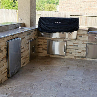 Outdoor kitchen with stone accents, stainless steel appliances, and a grill under a black cover.