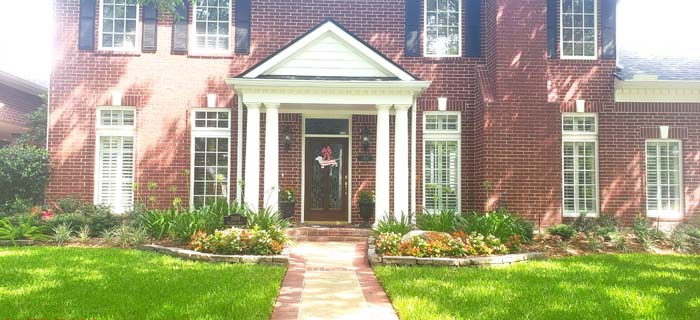 Red brick house with white columns, windows, and green lawn.