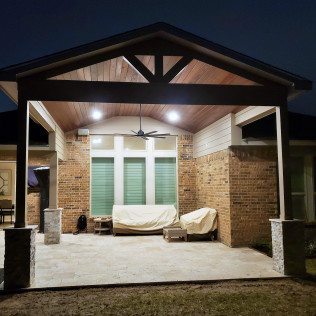 Covered patio with lights, seating, and brick wall at dusk.