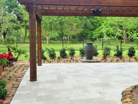 Patio with wooden pergola, stone pavers, lush greenery, and a decorative fountain.