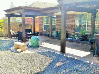 Patio with a pergola, furniture, and landscaping, featuring brick home backdrop and a stone bench.