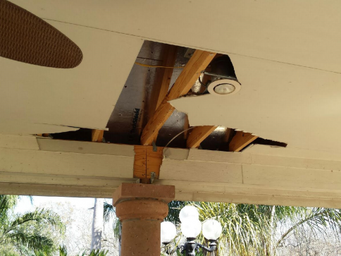 Damaged ceiling with a large hole revealing wooden beams, a light fixture, and a support column below.