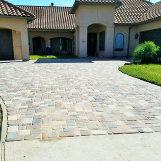 Brick paved driveway leading to a house with a beige exterior and a tile roof.