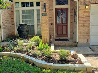 Brick home with a landscaped front yard.  A decorative vase sits near a window, with a wooden door.