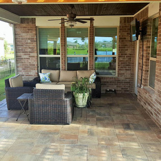 Outdoor patio with wicker furniture, brick walls, and a view of a lake through windows.