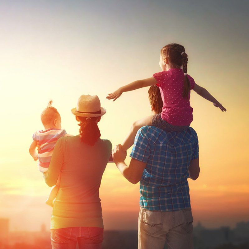 A man is carrying a little girl on his shoulders while a woman holds a baby.