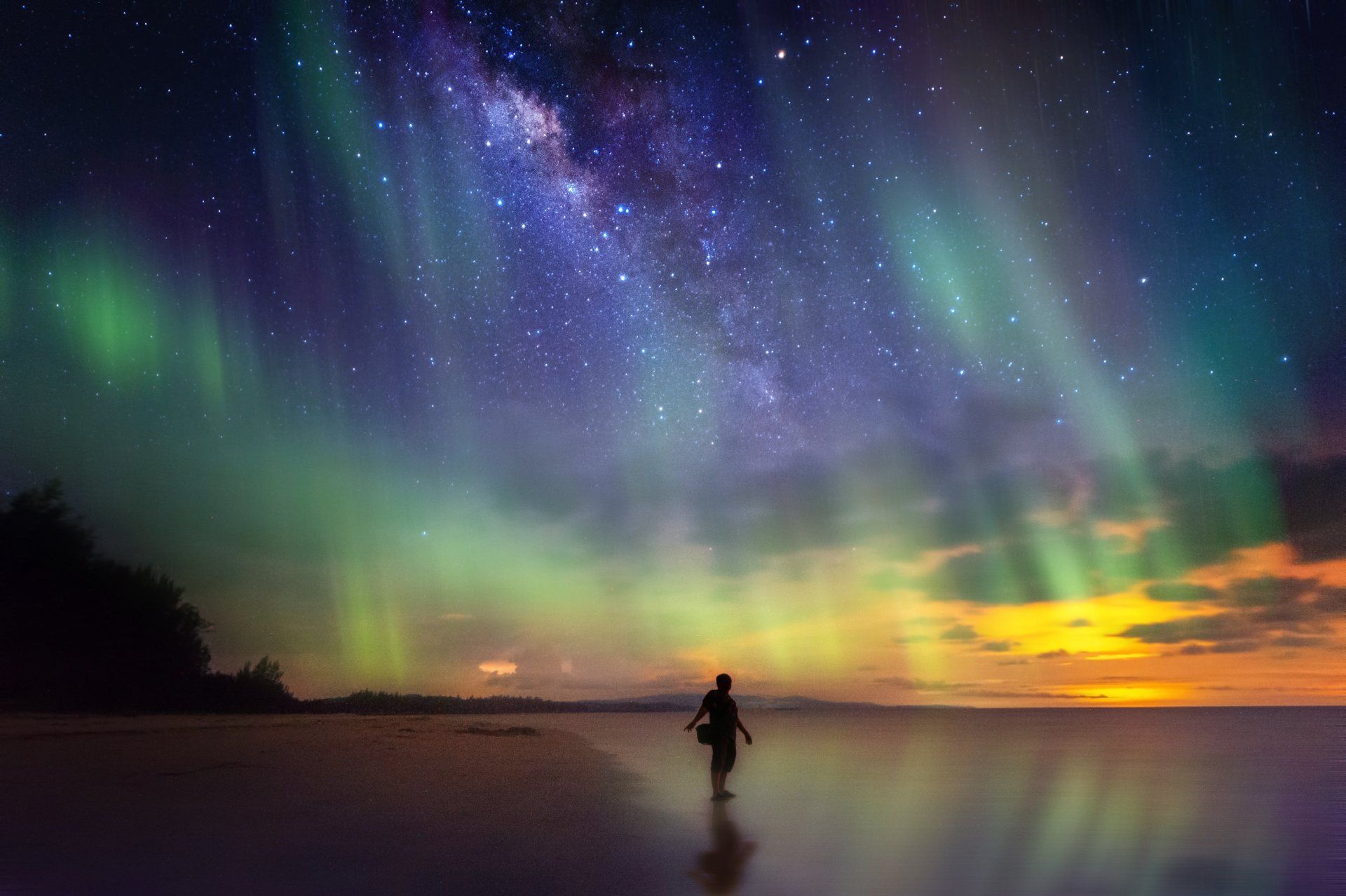 A person is standing on a beach under the aurora borealis.