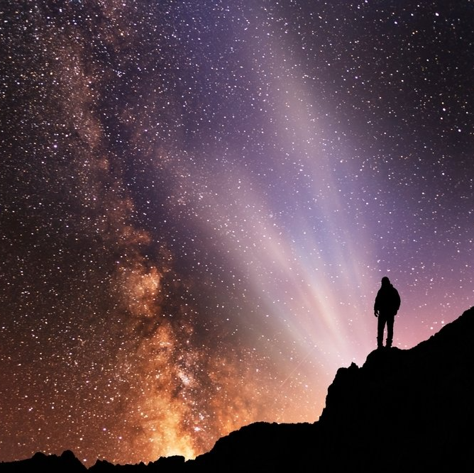 A person standing on top of a mountain looking at the stars