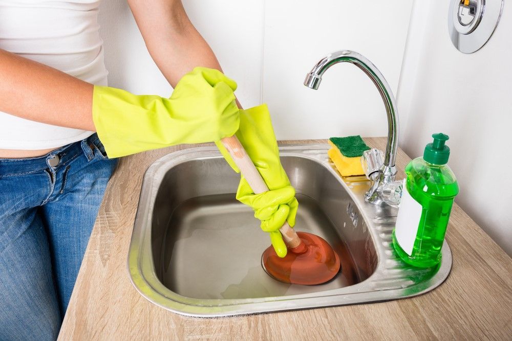 A woman is using a plunger to unblock a sink. Northglenn, Colorado accountable home services