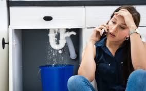 A woman is sitting on the floor under a sink talking on a cell phone. Northglenn, Colorado accountable home services