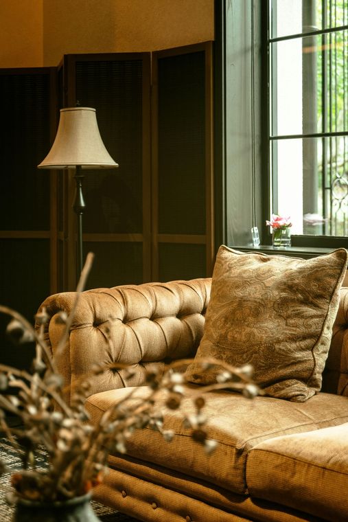 Sunlit living room with a tan tufted sofa, floor lamp, and large window.