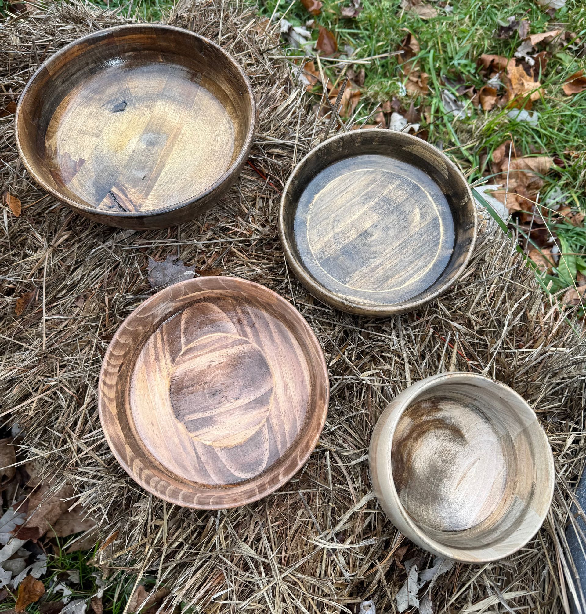 Four empty, round, wooden bowls sit on dried grass and leaves.
