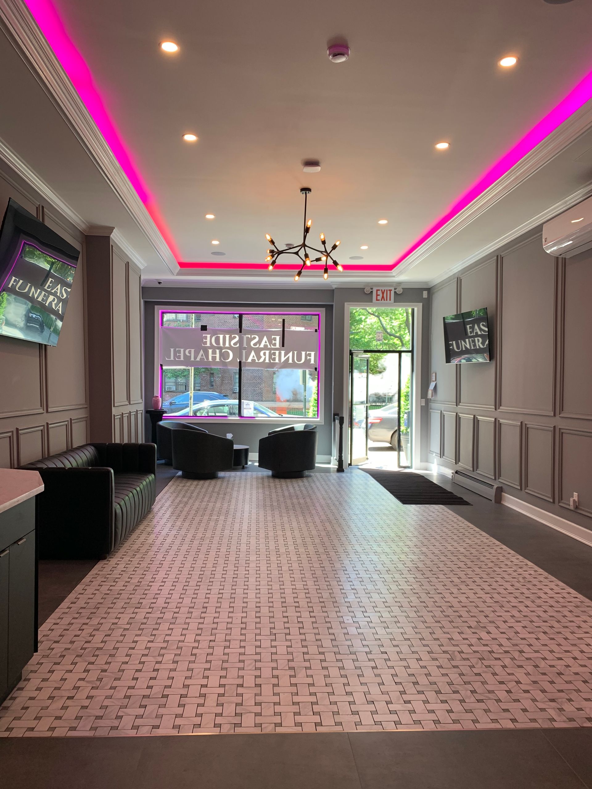 Empty event hall with pink ceiling lights, wall-mounted TVs, and an open doorway to the outside.