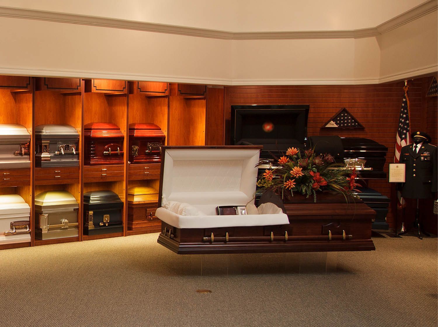 Open casket in a funeral home surrounded by flowers and display niches