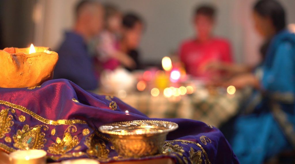 Lit candles on a purple cloth in the foreground, with blurred people gathered in the background.