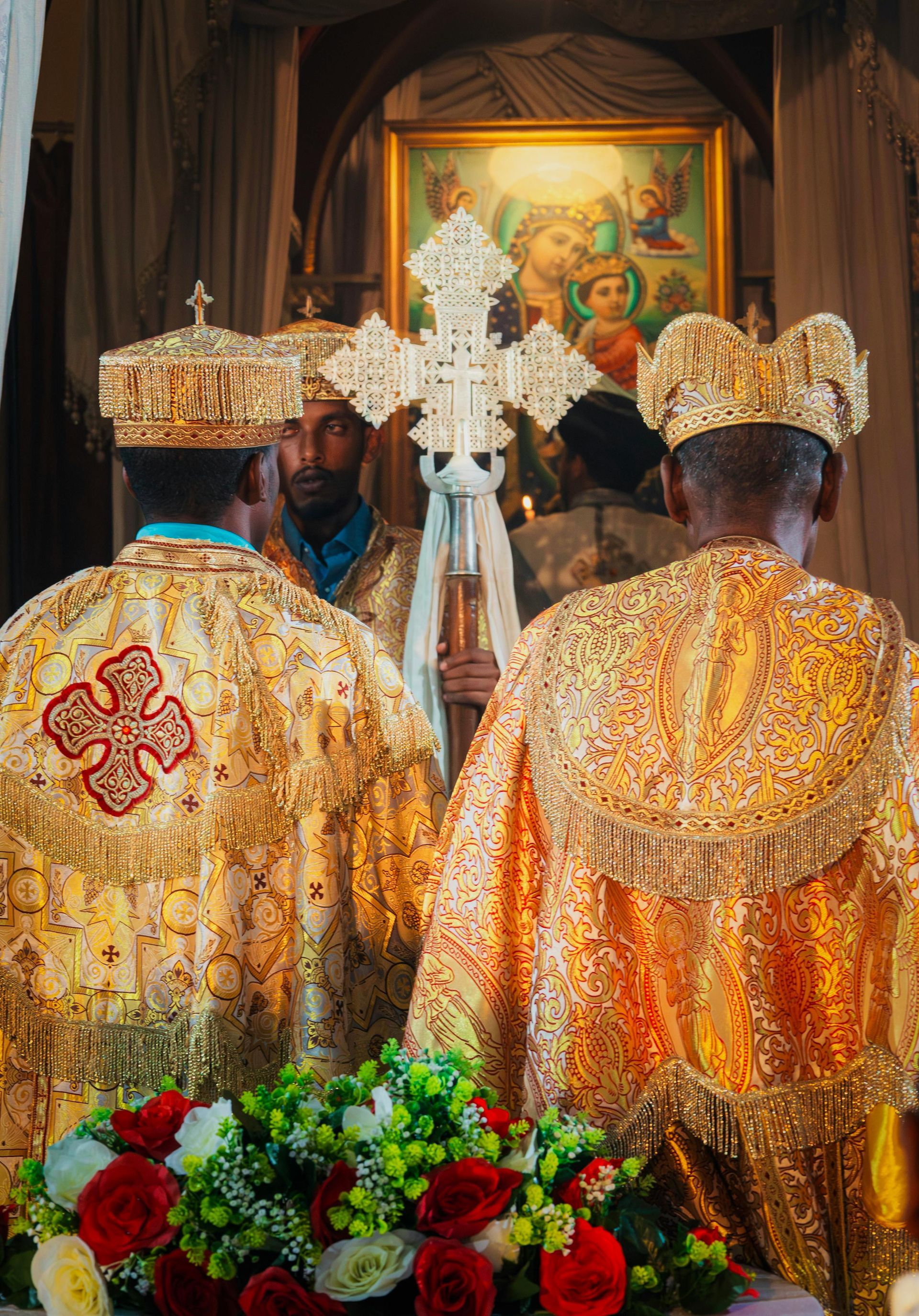 Three clergy in gold vestments before a decorated altar, with flowers in the foreground.