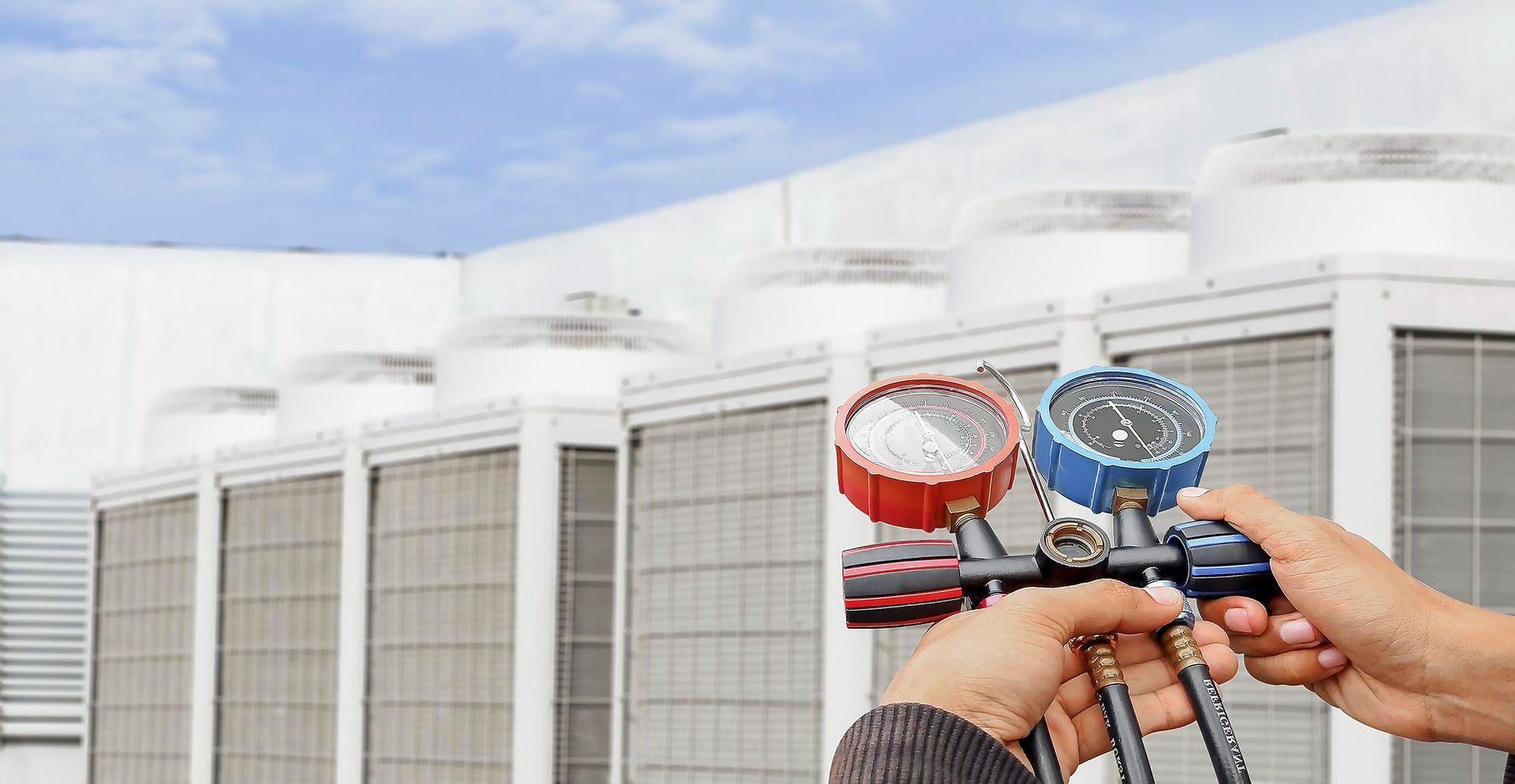 Two hands hold red and blue hose nozzles spraying water at an industrial building exterior