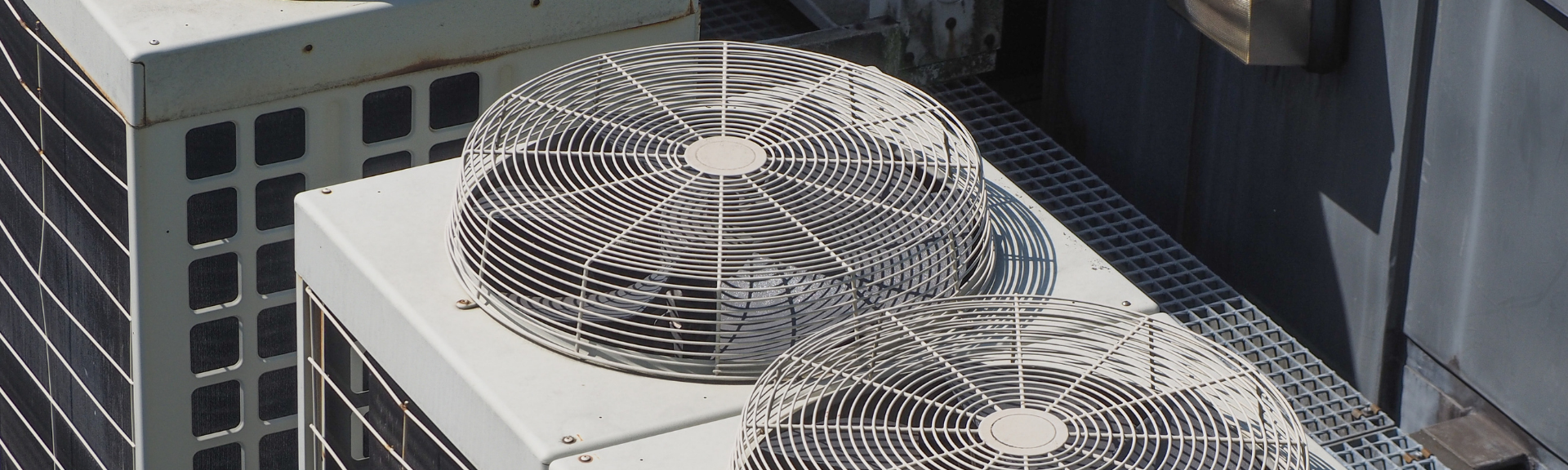 Two rooftop HVAC fans on a building next to tall windows and a dark wall