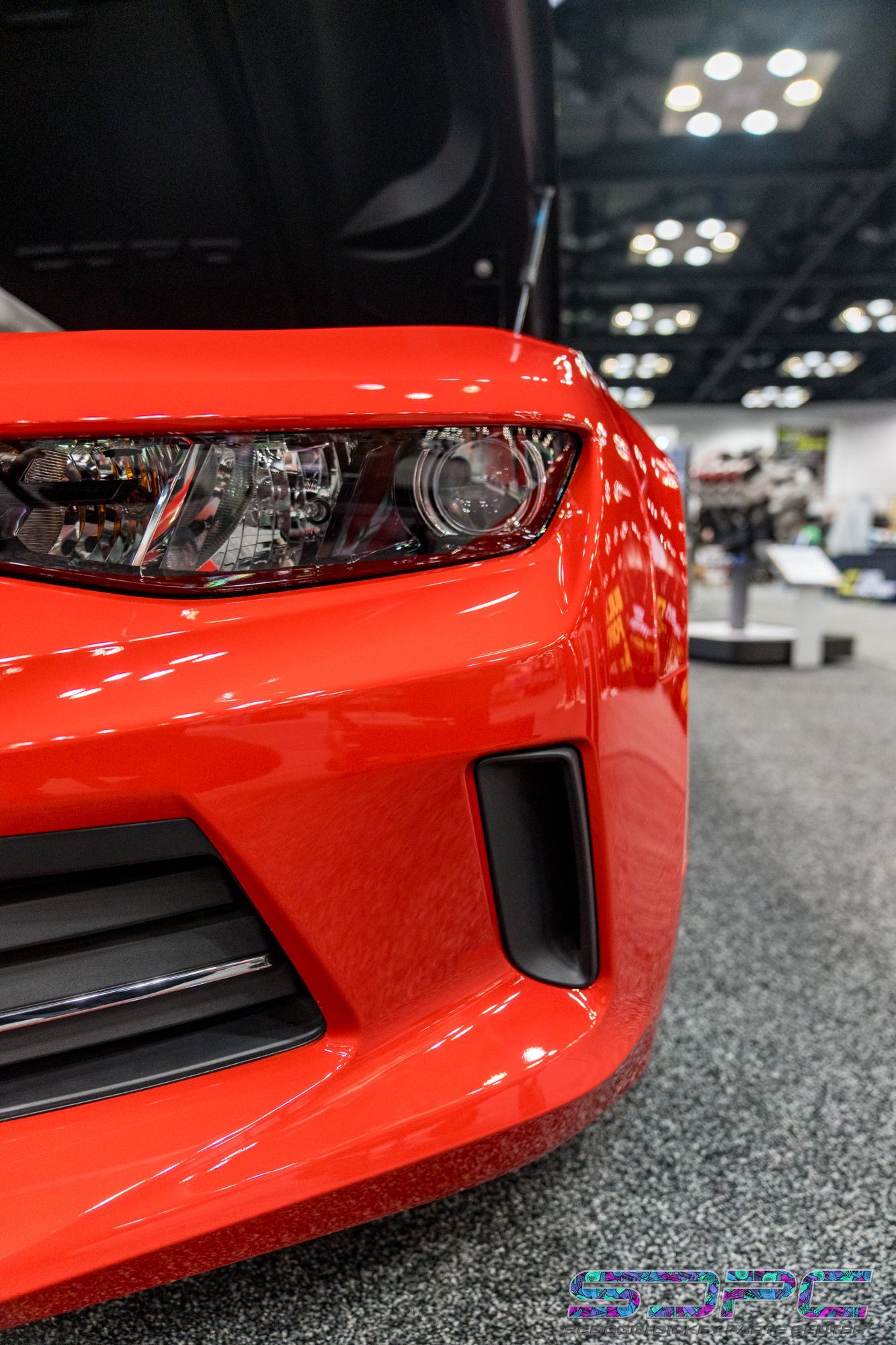 Red Chevrolet Camaro, partially visible with open hood, headlight and bumper detail.