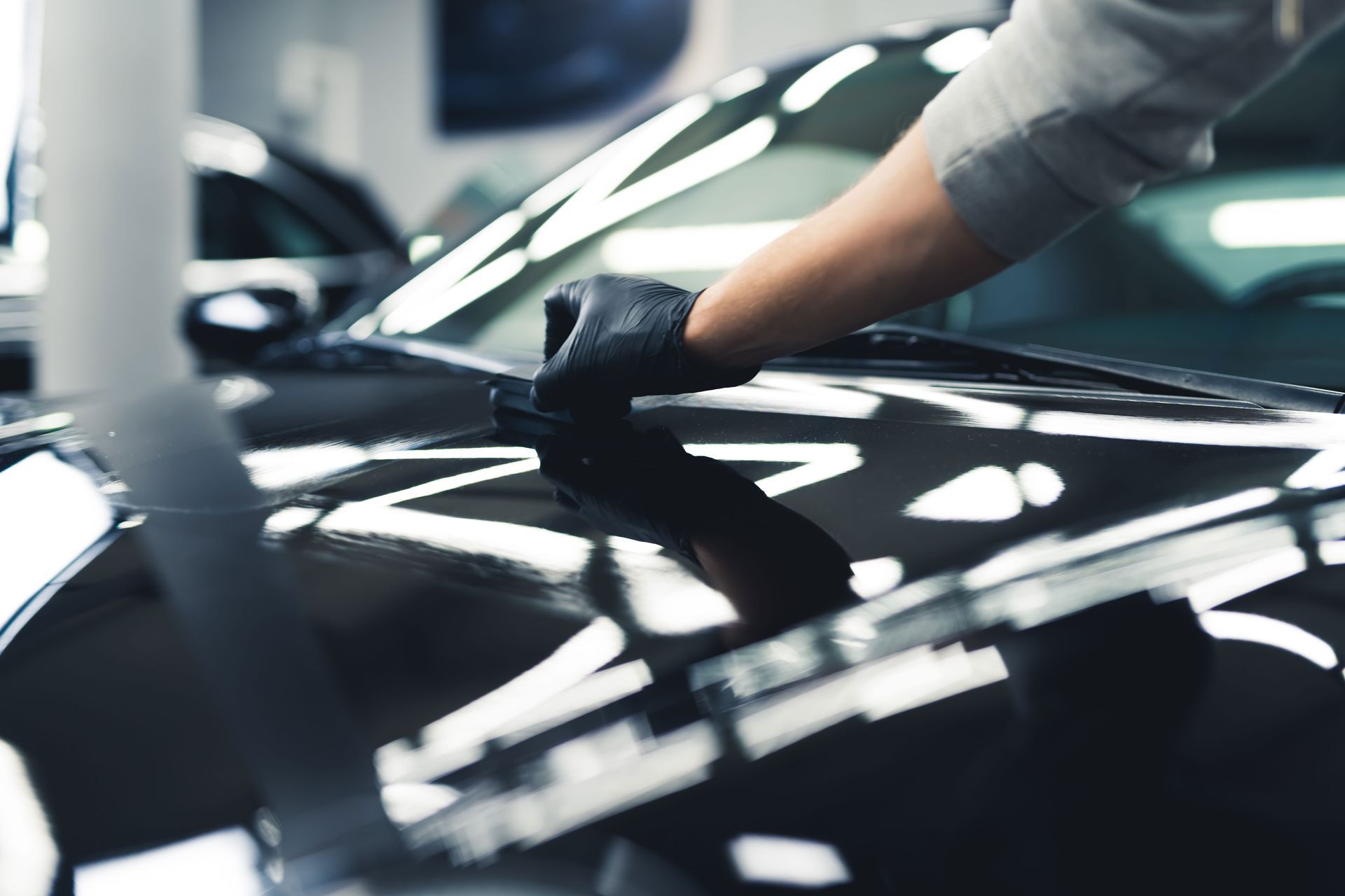 Person wearing black gloves applying wax to black car's hood.