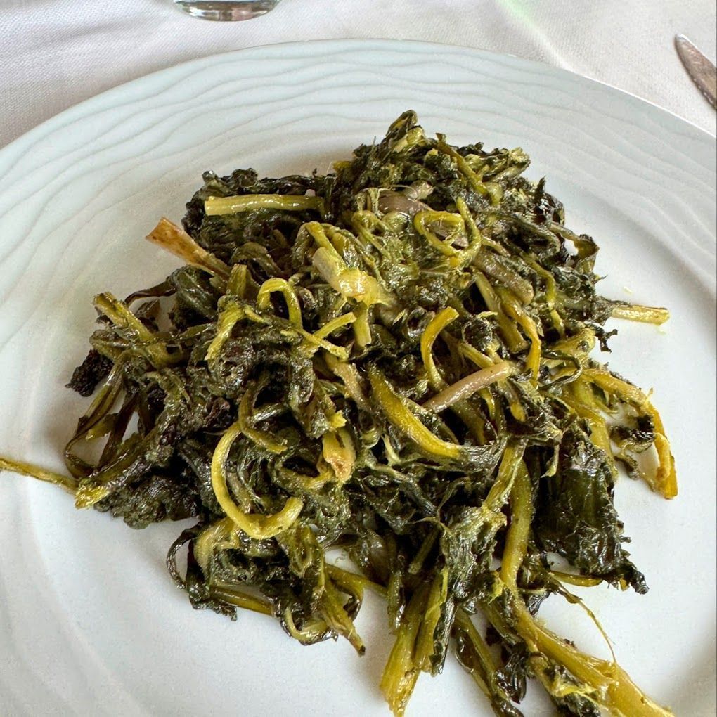 Piatto di pasta con pesto verde scuro e verdure appassite su un piatto bianco.