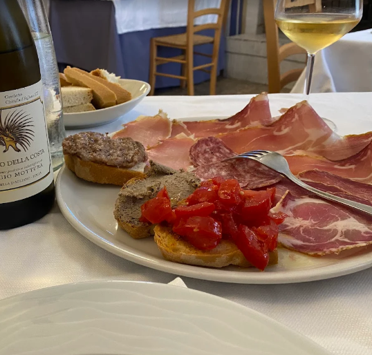 Vino e tapas su un tavolo, con salumi, pane e pomodori su un piatto bianco.