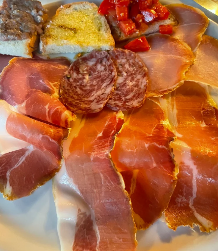 Piatto di salumi affettati con pane, formaggio e peperoni rossi su un piatto bianco.