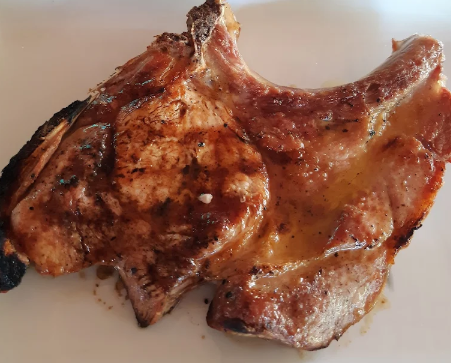 Braciola di maiale grigliata su un piatto bianco, dorata e lucida di salsa.