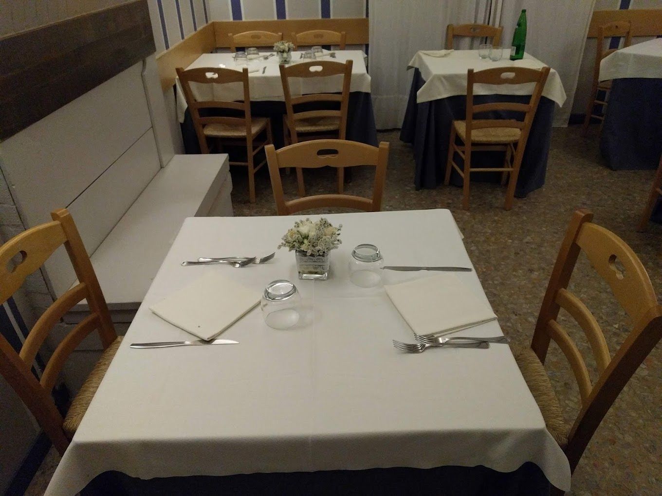 Piccola sala da pranzo di un ristorante con tovaglie bianche, sedie in legno e tavoli apparecchiati contro pareti piastrellate.