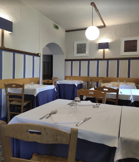Sala da pranzo vuota con tovaglie bianche, sedie di legno, finiture blu e un lampadario rotondo a sospensione.