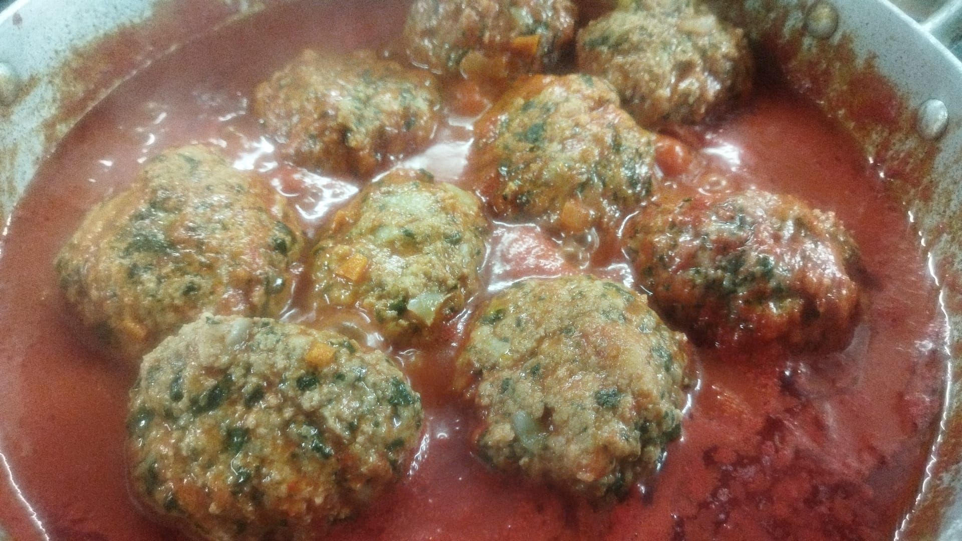 Polpette in salsa di pomodoro, guarnite con erbe aromatiche, in un piatto fondo.