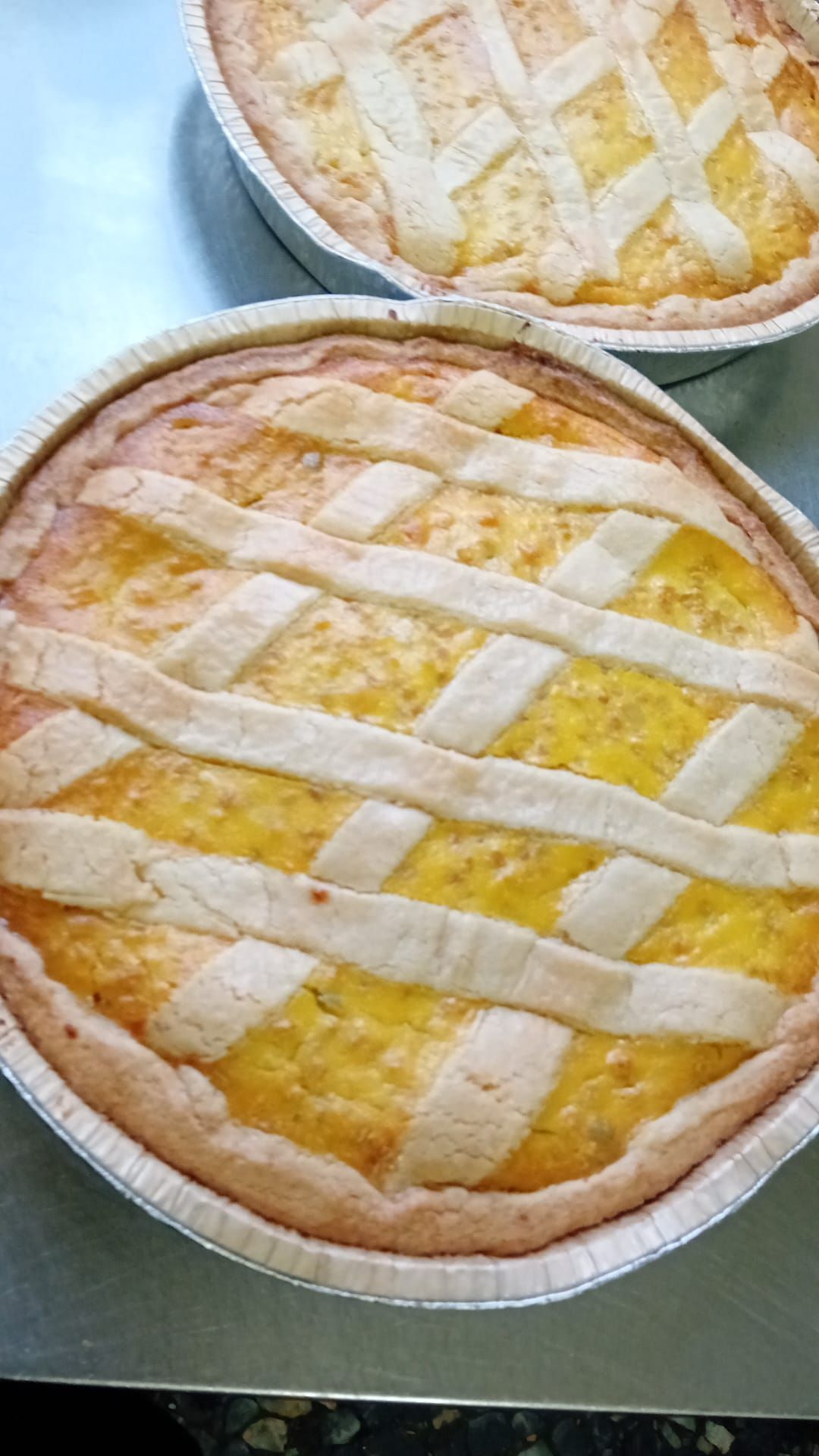 Due torte di frutta con copertura a griglia in teglie di alluminio su un piano di lavoro