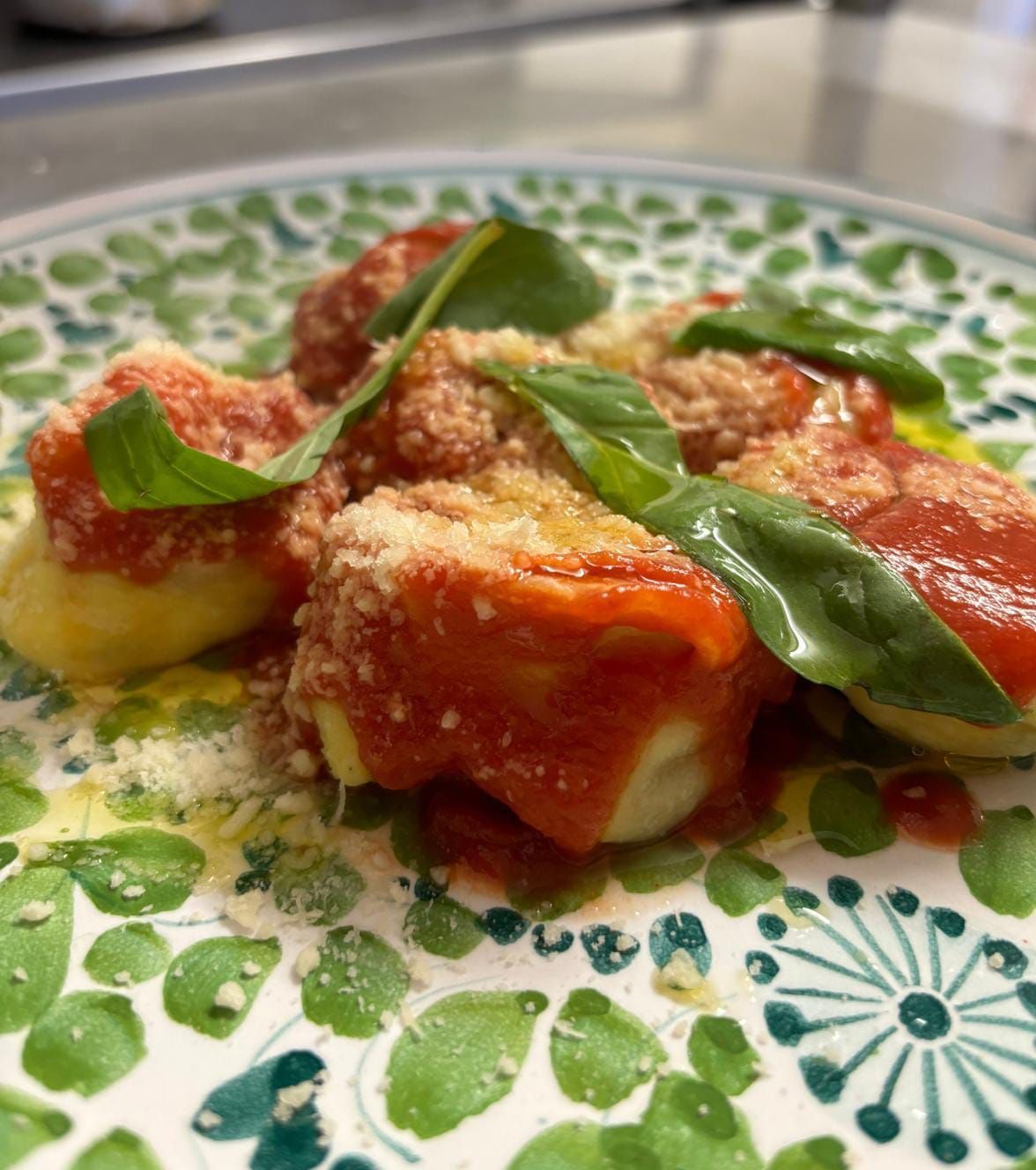 Piatto di ravioli con salsa di pomodoro, formaggio grattugiato e basilico fresco su un piatto decorato.