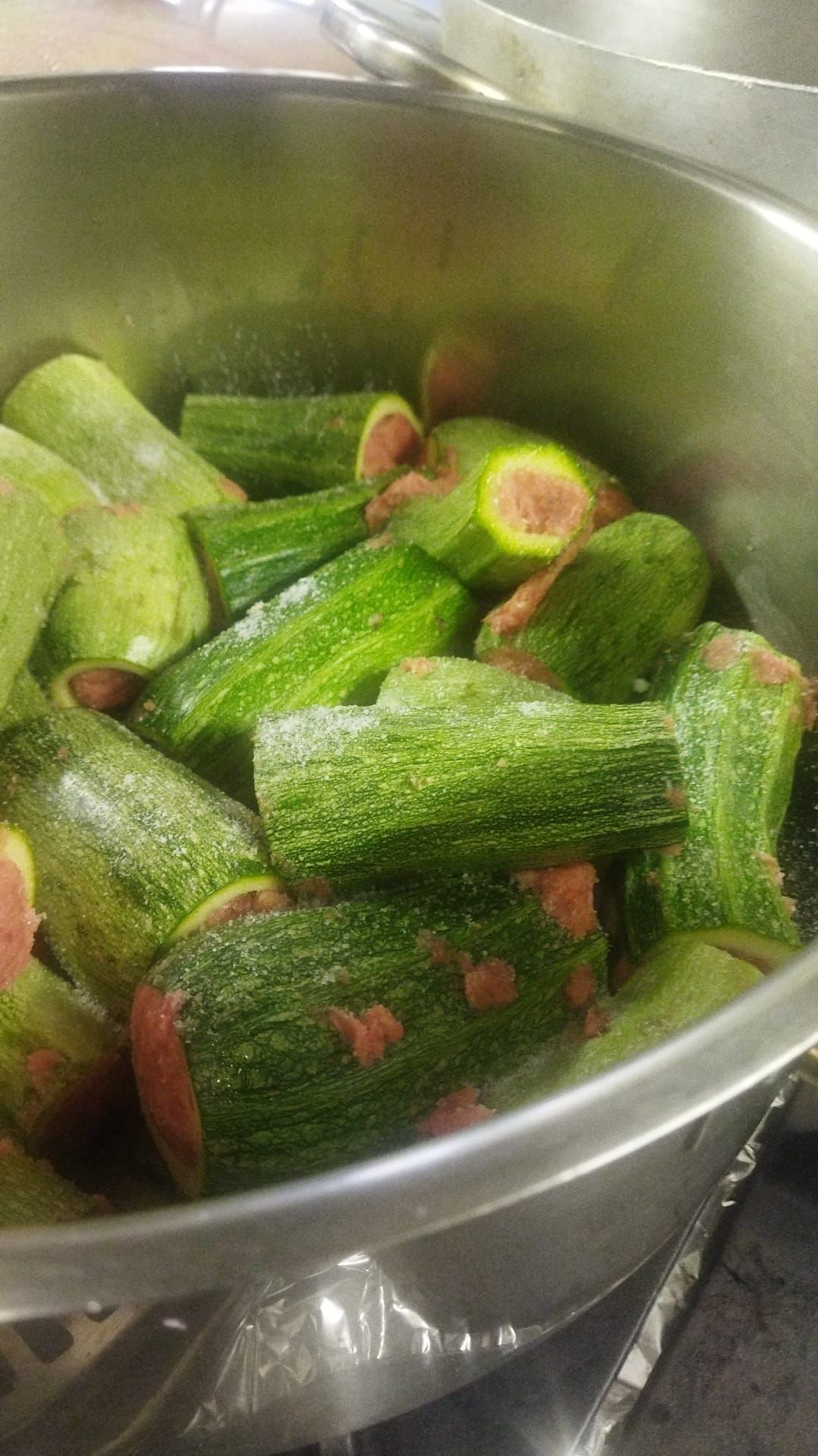 Pezzi di okra verde in una ciotola di metallo, con visibili alcune spezie rosse o peperoni.