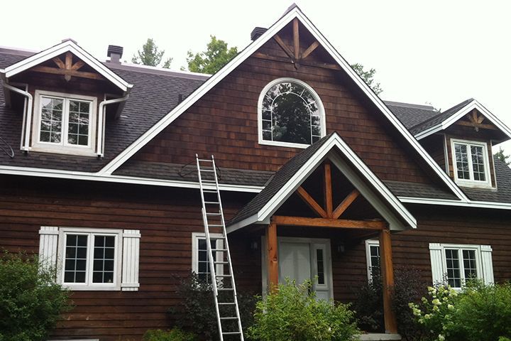 Brown house with white trim, arched window, and ladder leaning against the roof.