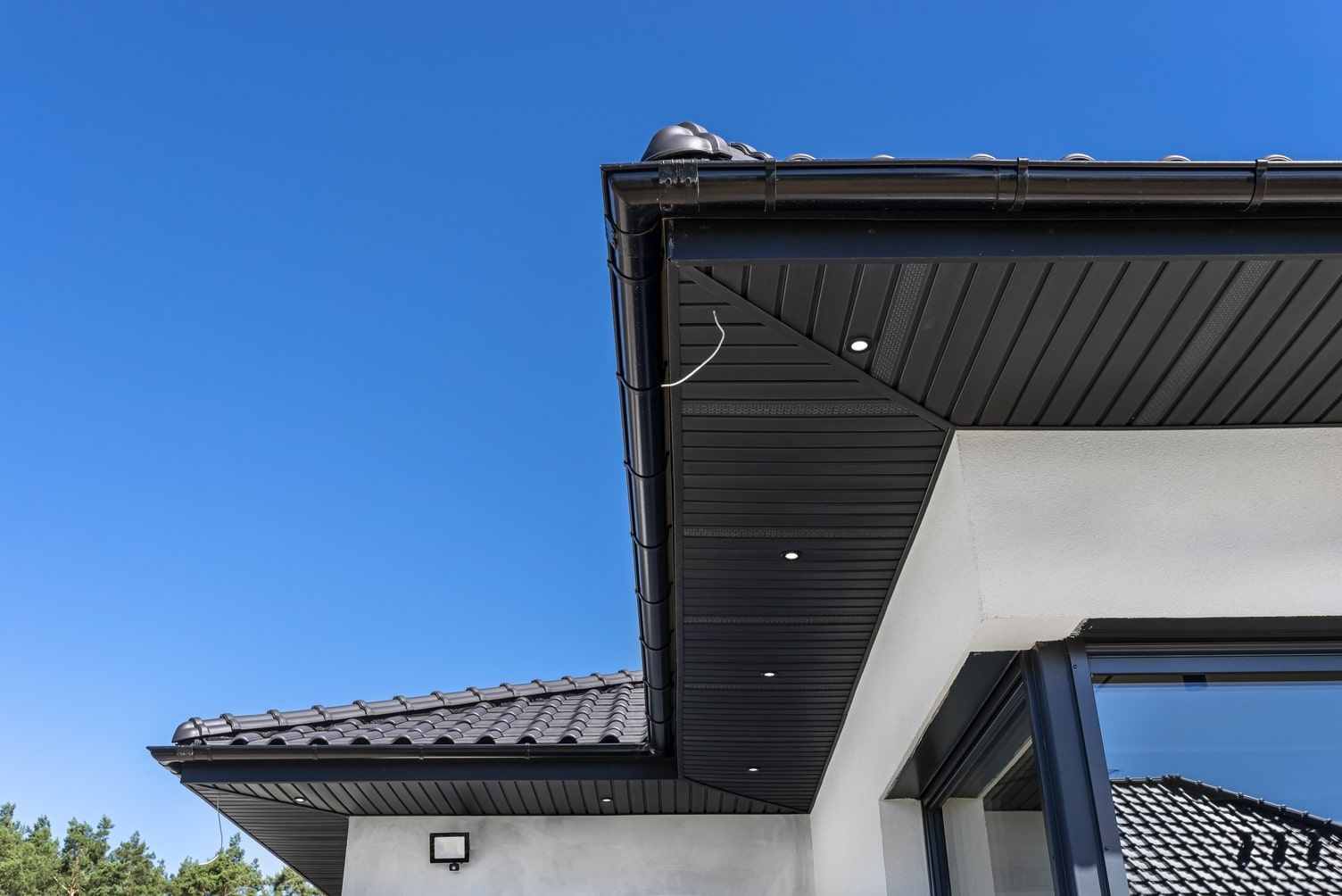 Corner of a house with a black roof, eaves, and a window