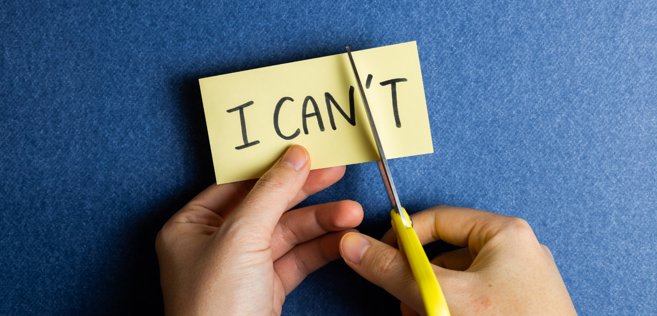 Hands with scissors cutting a yellow Post-it Sticky Note symbolizing overcoming self-limiting thoughts