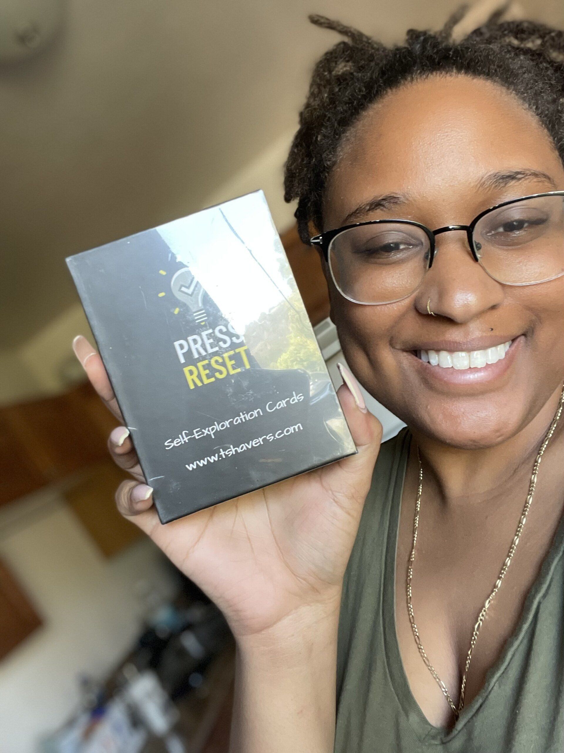 A successful young professional woman wearing glasses smiles while holding up her new Press Reset affirmation cards.