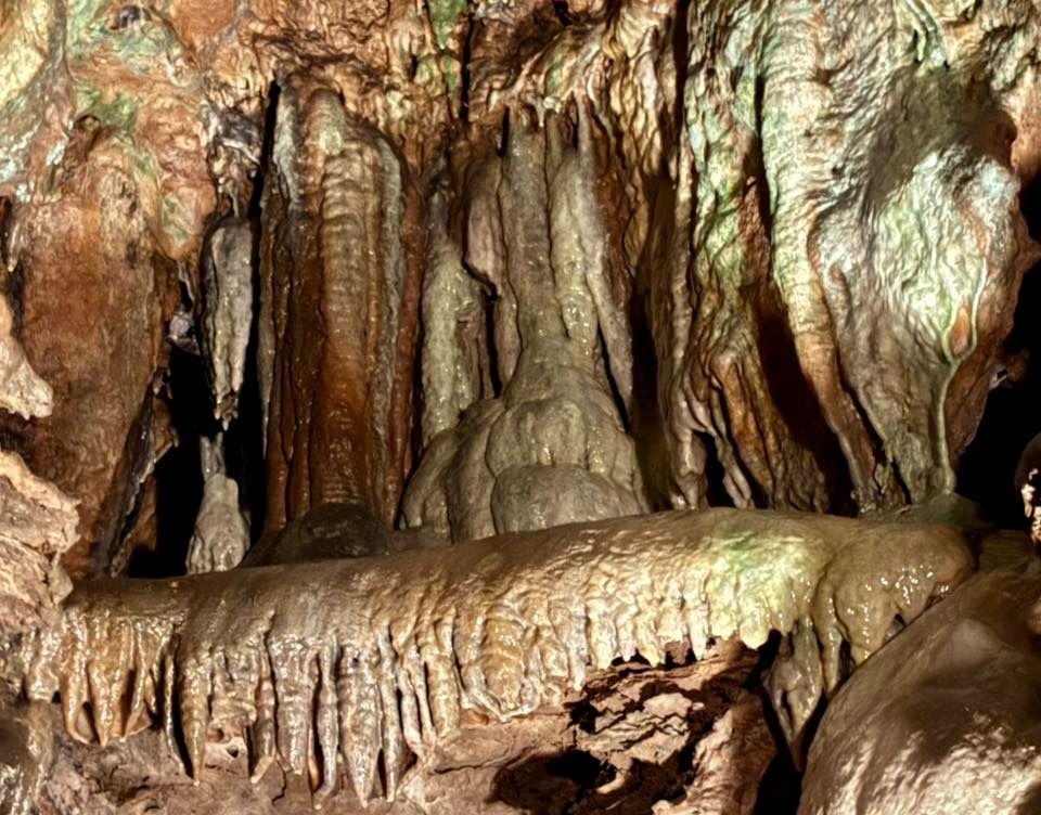 Cave interior with brown stalactites and a large, central rock formation.