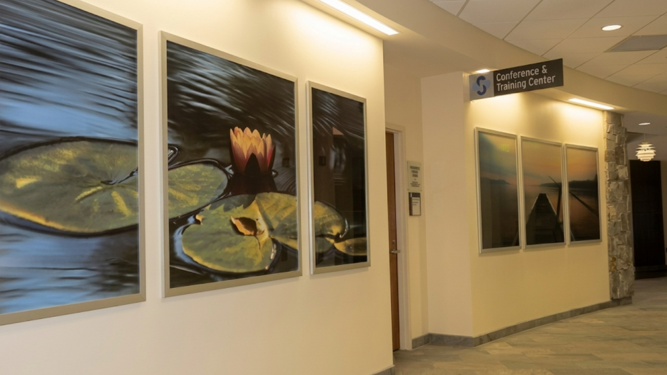 Hallway with framed abstract paintings and a corridor leading to a doorway under a hanging sign.